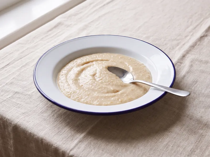 A bowl of smooth light brown breakfast cereal with a spoon