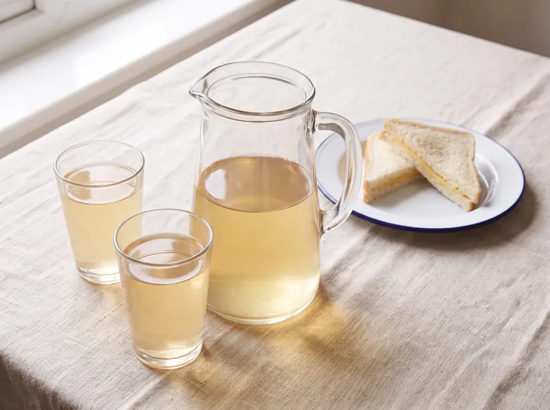 A glass jug of cordial mixed with water, with glasses on a lunch table